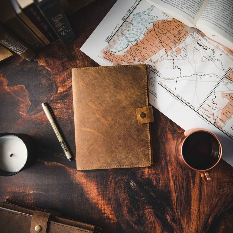 Leather journal on wooden table with travel accessories